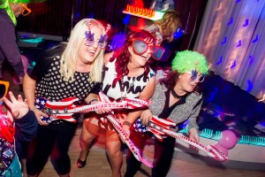 three women wearing oversized glasses and dancing in unison with balloon guitars